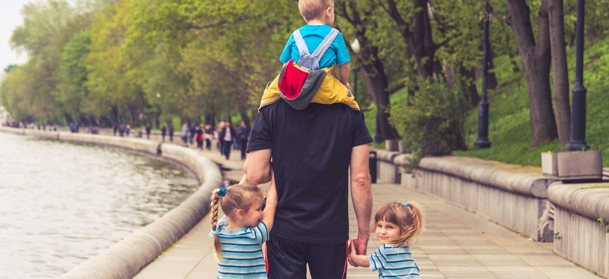 the father walks with three kids in the park